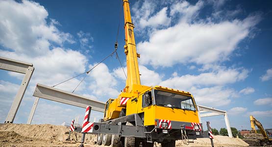 A mobile crane at a construction site lifting large concrete beams under a blue sky.