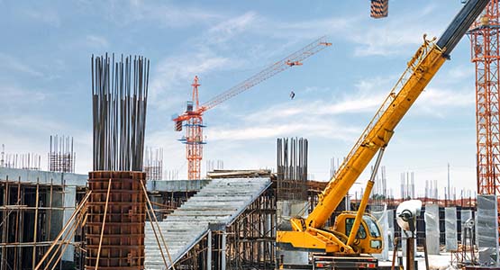 Construction site with cranes and scaffolding under a cloudy sky.